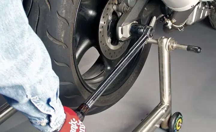 Mechanic using torque wrench on motorcycle rear wheel for maintenance.