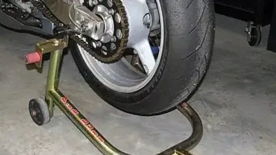 Motorcycle rear wheel on maintenance stand, showcasing chain and tire details in a garage setting.