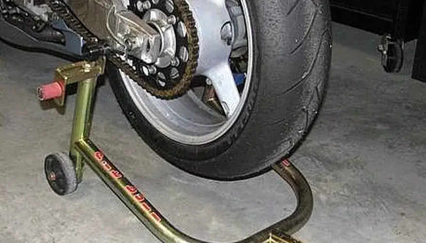 Motorcycle rear wheel on maintenance stand, showcasing chain and tire details in a garage setting.