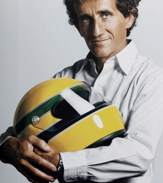 Прост - Engine Stories Man holding a yellow racing helmet, wearing a white shirt, smiling subtly.