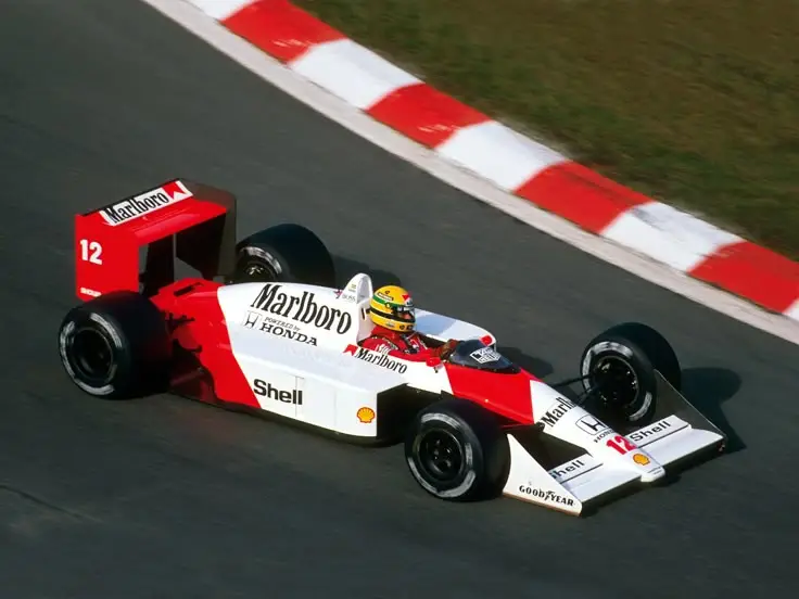 1988 McLaren-Honda MP4_4 - Engine Stories Red and white Formula 1 car with driver on track, featuring sponsorship logos, navigating a curve.