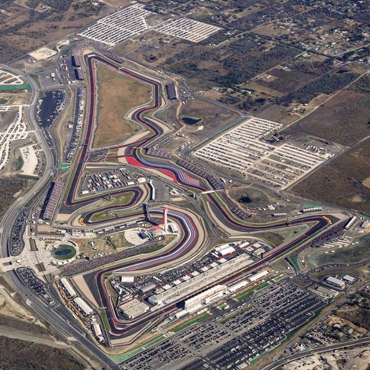 44 redjet Arrived in Austin at Circuit of The - Engine Stories Aerial view of a racetrack with winding circuits, grandstands, and parking area, showcasing a large motorsport complex amidst surrounding land.