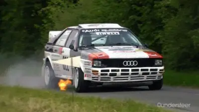 Rally car speeding on a track, flames visible from exhaust, showcasing dynamic motion and performance.