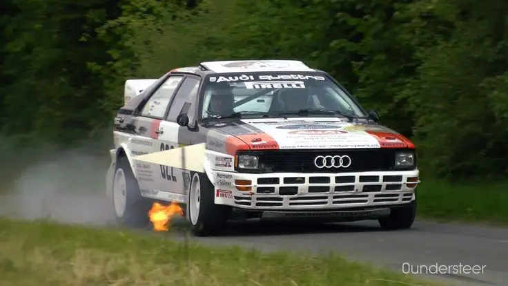 Rally car speeding on a track, flames visible from exhaust, showcasing dynamic motion and performance.