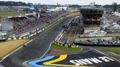 Le Mans racetrack view with crowd-filled stands and iconic curves, showcasing the vibrant atmosphere of a motorsport event.