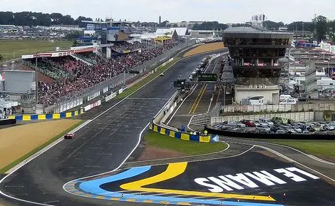 Le Mans racetrack view with crowd-filled stands and iconic curves, showcasing the vibrant atmosphere of a motorsport event.