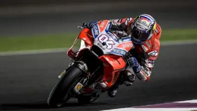 Motorcyclist in red gear racing on a track, leaning sharply into a turn, showcasing speed and precision in motorsports.