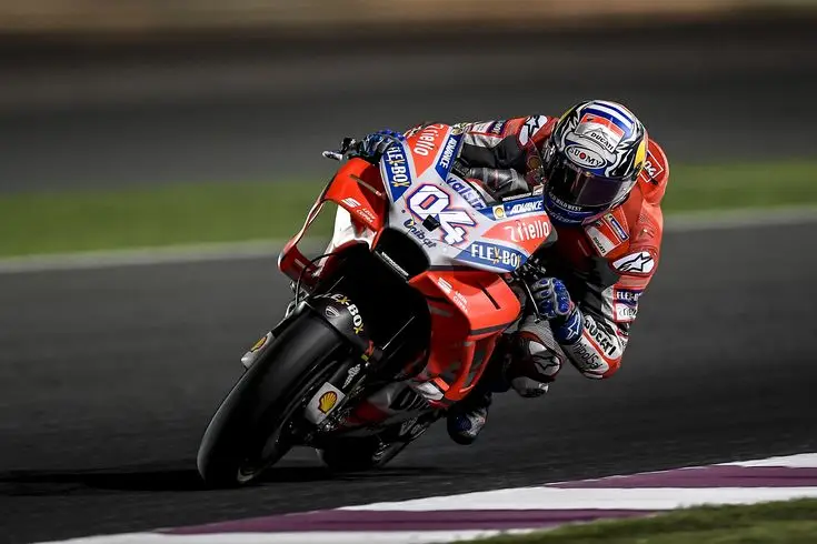Motorcyclist in red gear racing on a track, leaning sharply into a turn, showcasing speed and precision in motorsports.