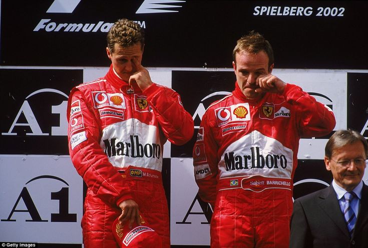 F1 AUSTRIAN GP MEMORIES_ Ferrari duo land in hot water and more - Engine Stories Ferrari F1 drivers on podium at Spielberg 2002, showing emotions in racing suits with sponsor logos.