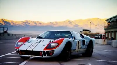 Vintage race car on a track at sunset with mountains in the background. Classic design and vibrant colors stand out.