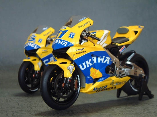Yellow and blue Honda racing bikes with detailed decals on a gray backdrop.