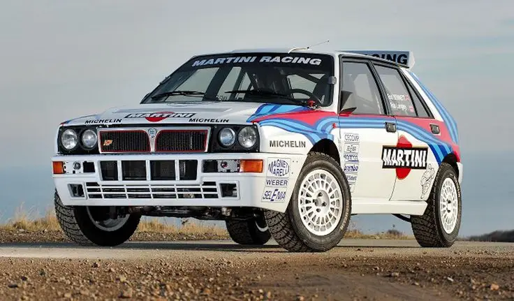 Classic rally car with Martini Racing livery on a gravel road, showcasing iconic design and performance elements.