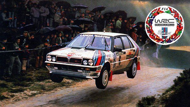 Rally car in mid-air during race, surrounded by spectators on a dirt track; WRC logo visible.