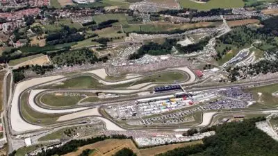 Aerial view of a bustling racetrack with winding circuits, surrounded by lush greenery and spectator stands.