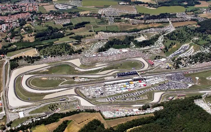 Aerial view of a bustling racetrack with winding circuits, surrounded by lush greenery and spectator stands.