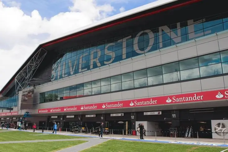 Race track garage at Silverstone Circuit, with bright sky above and people walking by, highlighting motorsport ambiance.