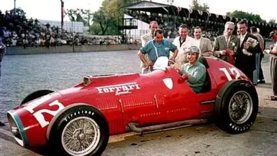 Vintage Ferrari race car with driver and crew at a racetrack, showcasing classic design and automotive heritage.