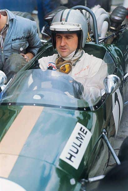 Race car driver in a green vintage Formula One car, wearing a helmet and goggles, ready for the track. Vintage motorsport scene.
