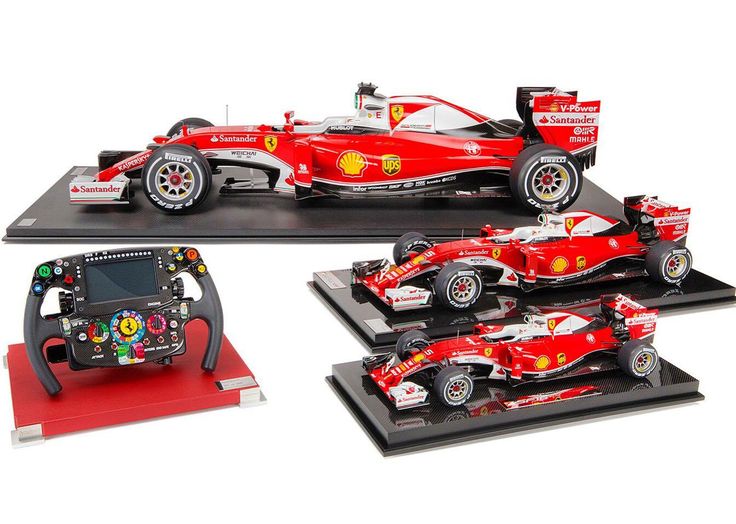 Ferrari F1 model cars and steering wheel display, featuring detailed sponsor logos and vibrant red liveries.