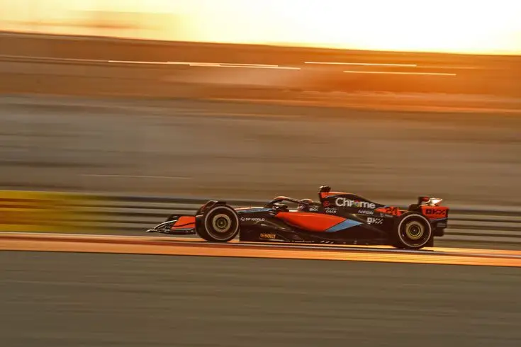 Formula 1 car speeding on track at sunset, emphasizing speed and motion against a golden sky backdrop.