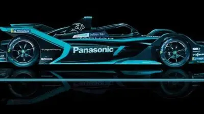 Jaguar Formula E race car in sleek black and teal design, side view with Panasonic branding, reflecting on shiny surface.