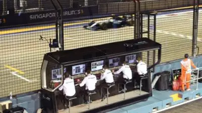 Mercedes AMG Petronas team monitors F1 race on screens at Singapore GP circuit as car speeds by on well-lit track.