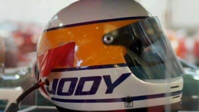 Racing helmet with JODY inscription, showcasing vibrant colors and visor, displayed in a museum setting.