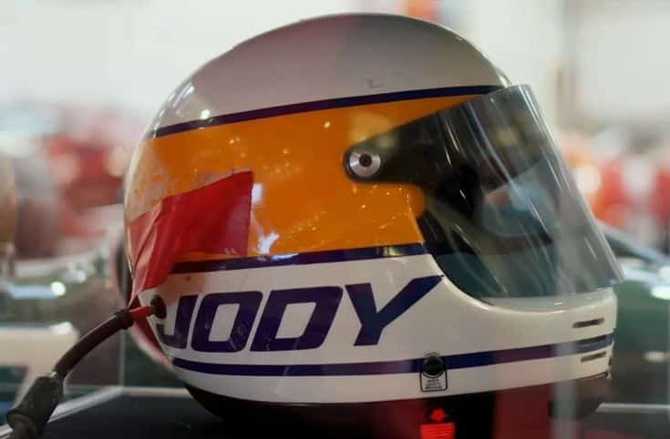 Racing helmet with JODY inscription, showcasing vibrant colors and visor, displayed in a museum setting.