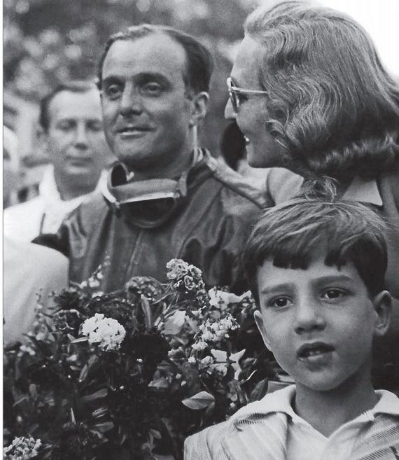 Vintage photo of a group celebrating, featuring a man with goggles and a young boy holding flowers. Retro, joyful moment.