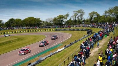 Race cars speed around a track surrounded by a crowd of spectators under a clear blue sky.