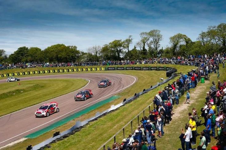 Race cars speed around a track surrounded by a crowd of spectators under a clear blue sky.