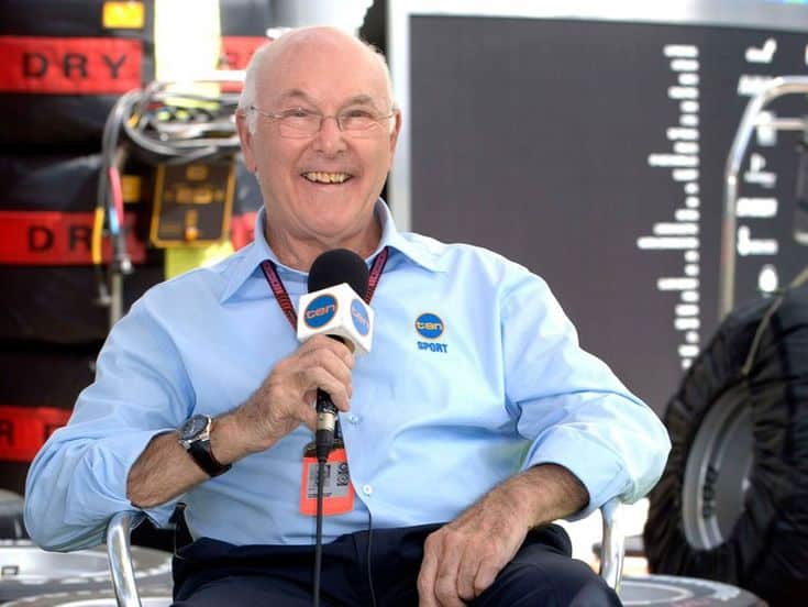 Man holding a microphone in a sports broadcasting setting, smiling, and wearing a blue shirt with a ten sport logo.