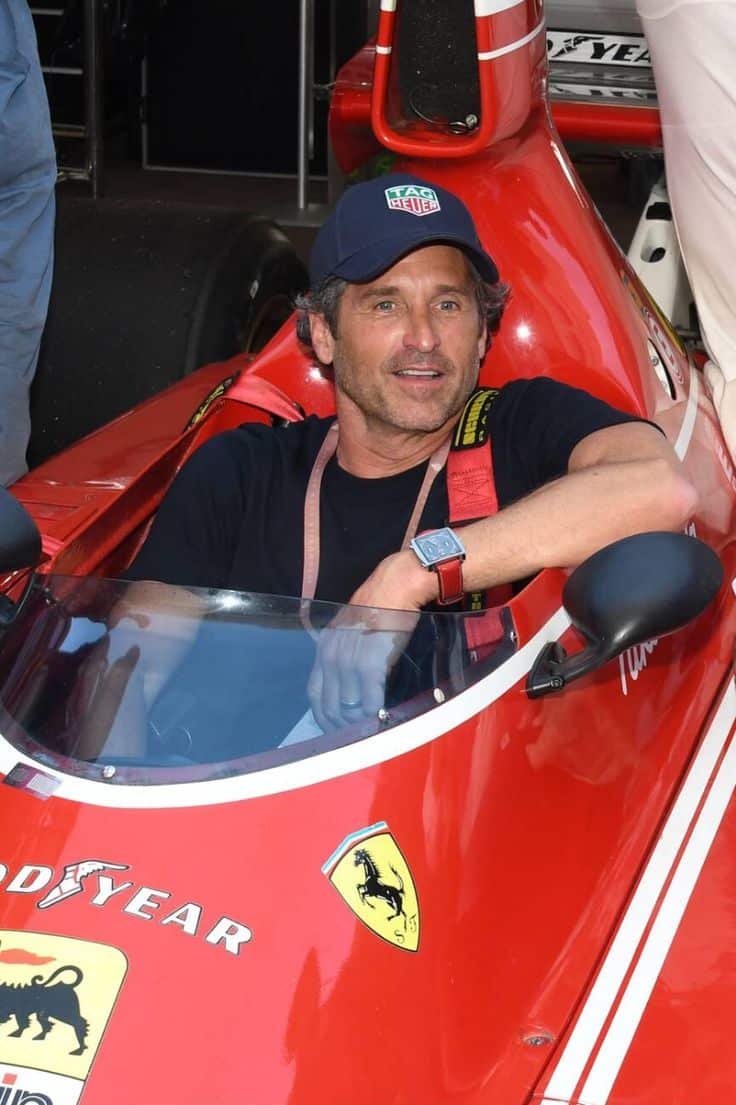 Man sitting in a classic red Ferrari race car, wearing a navy cap and black shirt, showcasing motorsport passion.