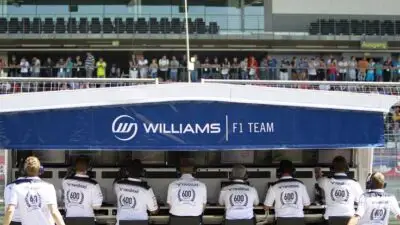Williams F1 Team crew at the trackside control station during a race weekend, with team branding and spectators in the background.