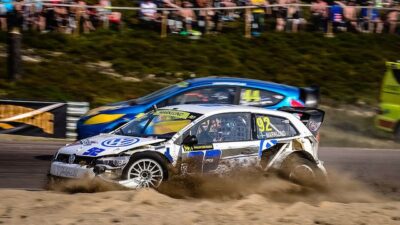 Rallycross race action with two cars speeding on a dirt track, surrounded by spectators, highlighting dynamic motorsport excitement.