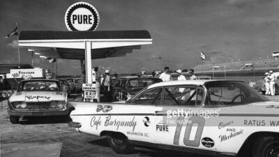 Vintage race cars refuel at a Pure gas station during a classic auto race, highlighting 1960s racing culture and sponsorship.