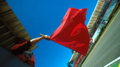Race official waving a red flag on a sunny day at a racetrack, signaling a stop in the competition for safety.