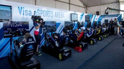People competing in virtual racing at Visa eSports Arena, surrounded by screens and cameras under a white tent.