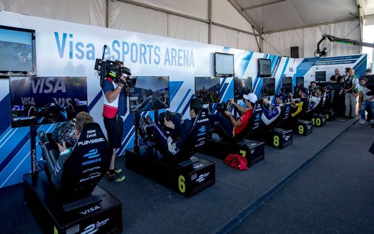 People competing in virtual racing at Visa eSports Arena, surrounded by screens and cameras under a white tent.