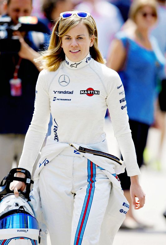 Female race car driver in white racing suit holding helmet, ready for track. Racing style and determination.