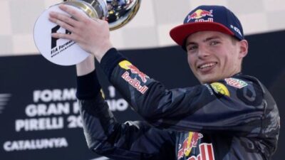 Race car driver celebrating with trophy in FIA Formula 1 event, wearing a Red Bull Racing suit and cap, at Gran Premio de Catalunya.