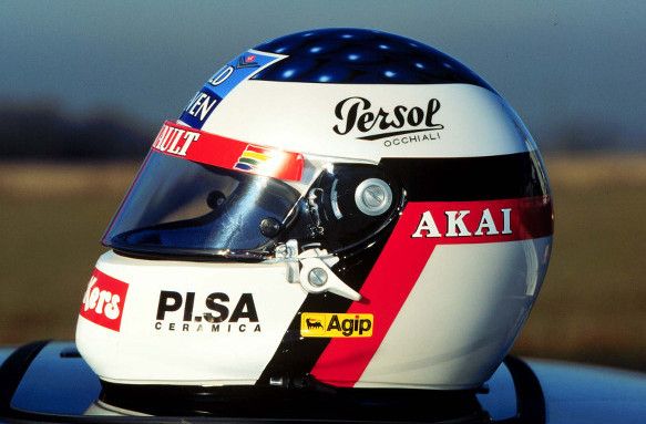 White and blue racing helmet with sponsor logos including Persol, Akai, and Agip, against a blurred background.