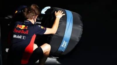 Person in racing team uniform handling a wrapped Formula 1 tire, emphasizing preparation and focus.