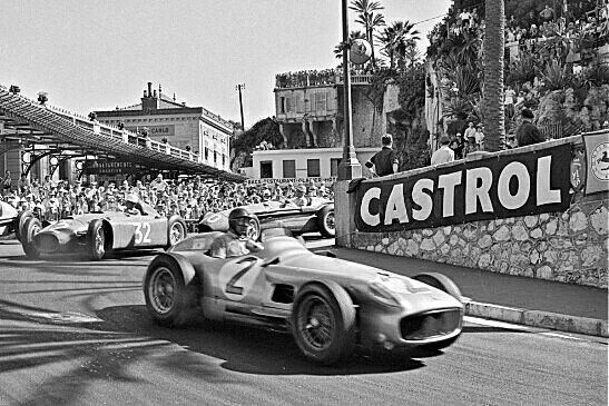 Vintage car race with classic vehicles on a street circuit, drivers navigating a turn, surrounded by spectators and Castrol signage.