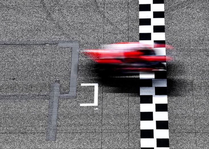 Blurred red race car crossing finish line on checkered asphalt track, showcasing speed and competition.