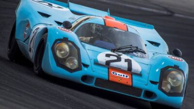 Vintage blue race car with number 21 and Gulf branding speeding on a racetrack.