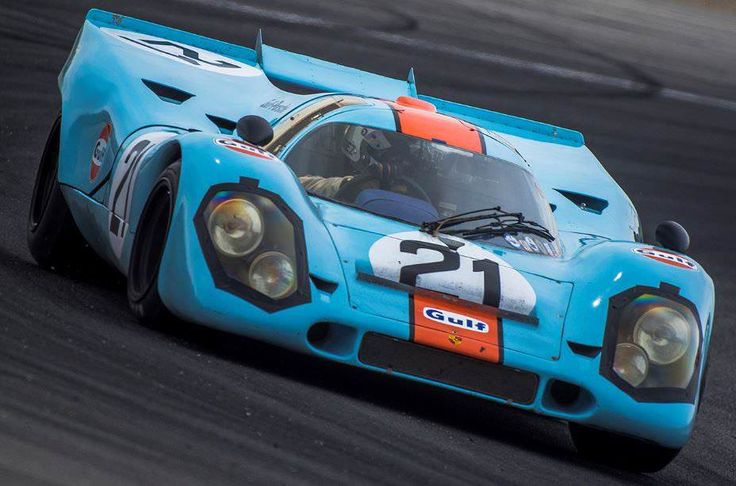 Vintage blue race car with number 21 and Gulf branding speeding on a racetrack.