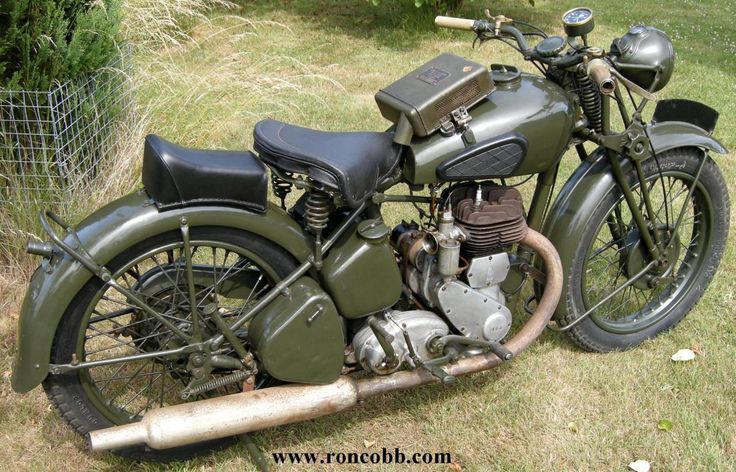 Vintage military motorcycle with green paint, parked on grass. Features classic design and exposed engine components.