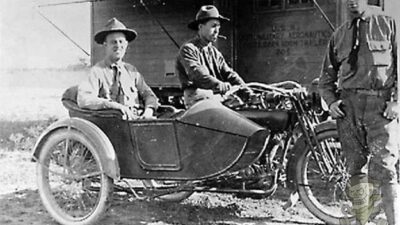 Three men pose with a vintage motorcycle and sidecar outdoors, showcasing early 20th-century transportation.