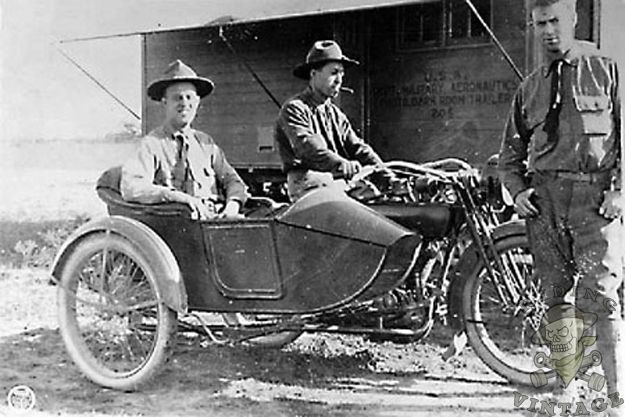 Three men pose with a vintage motorcycle and sidecar outdoors, showcasing early 20th-century transportation.
